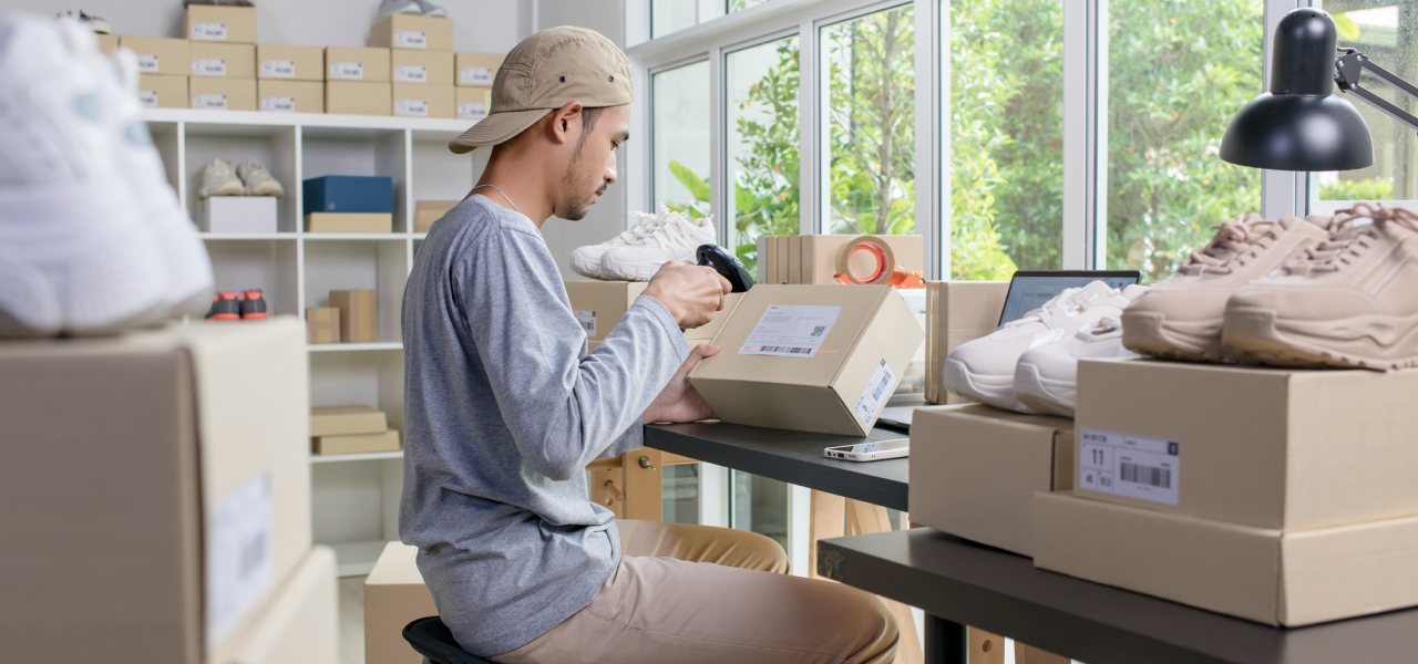A young man scans a label on a shipping box in a room full of boxes.