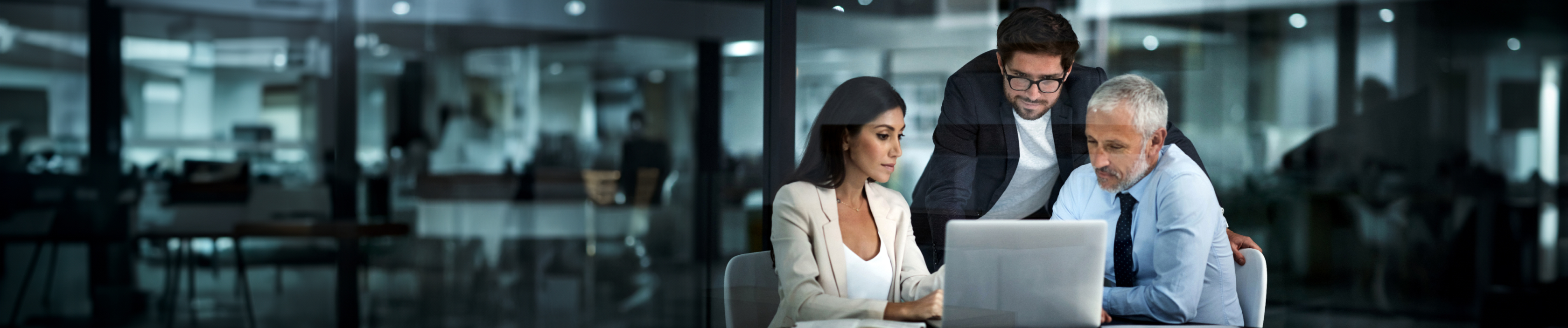 Three people are gathered around a laptop in an office.
