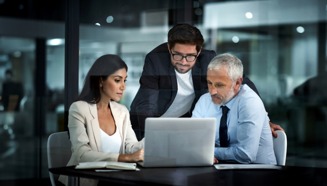 Three people are gathered around a laptop in an office.