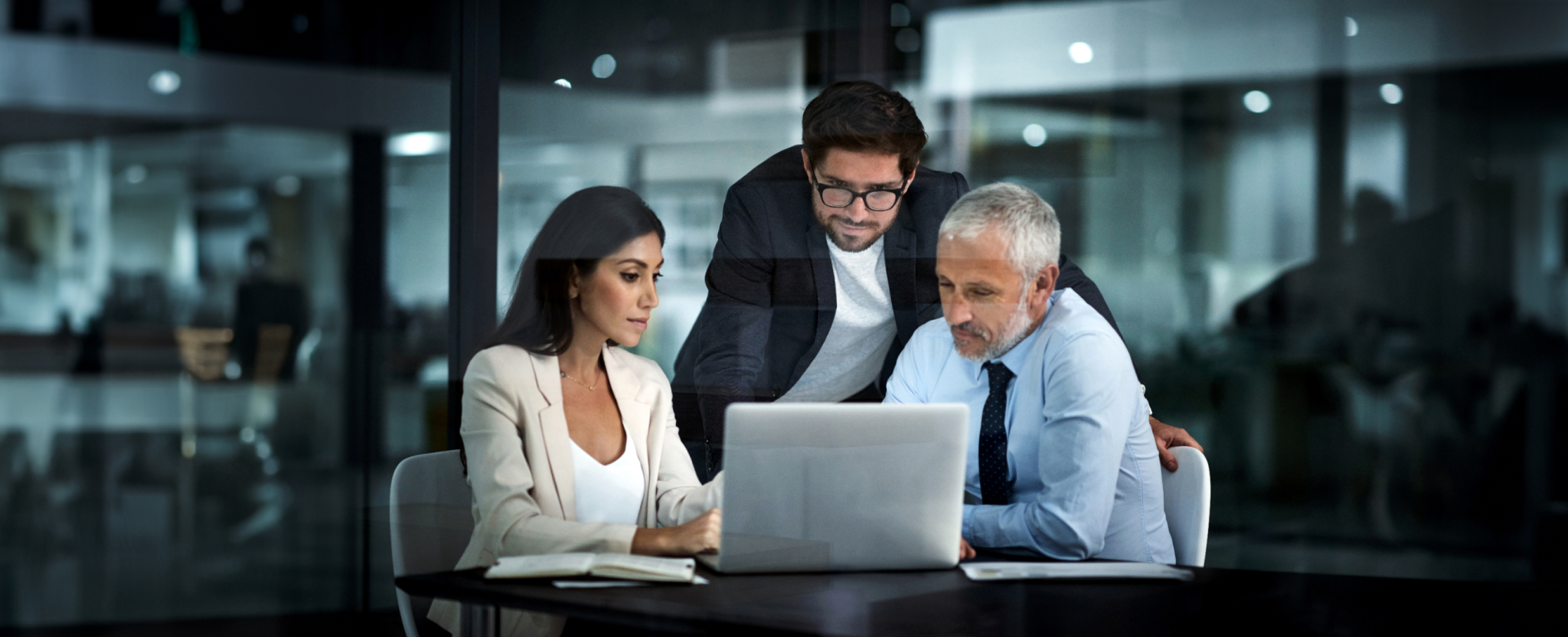Three people are gathered around a laptop in an office.