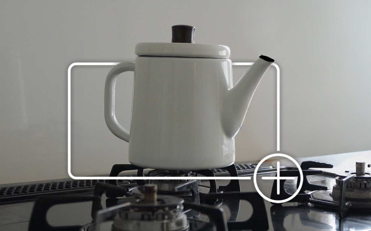 White enamel kettle on a gas stove burner framed by a white focus box with a plus icon indicating adding the item to an online shopping cart. White enamel kettle on a gas stove burner framed by a white focus box with a plus icon indicating adding the item to an online shopping cart.