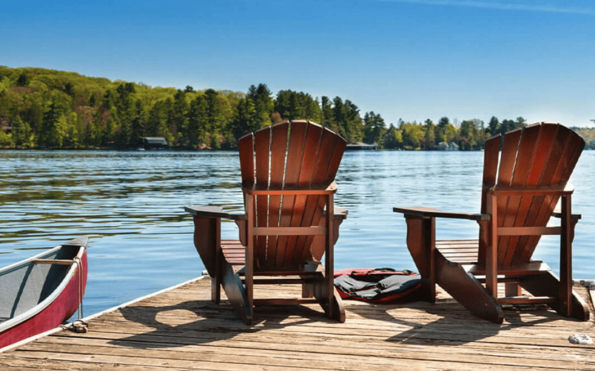 Two wooden chairs sit on a lakeside dock, next to a canoe. Two wooden chairs sit on a lakeside dock, next to a canoe.
