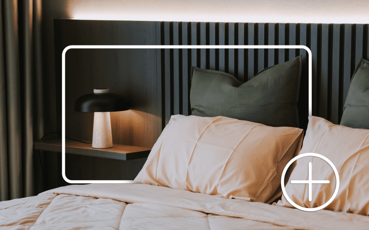 A bed with pillows, bedside table and lamp. Items are outlined by a white box and plus sign indicating adding to an online shopping cart. A bed with pillows, bedside table and lamp. Items are outlined by a white box and plus sign indicating adding to an online shopping cart.