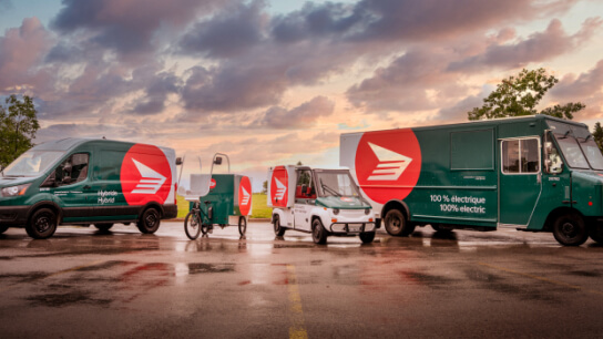 Canada Post hybrid and electric delivery vehicles parked in a row. Canada Post hybrid and electric delivery vehicles parked in a row.