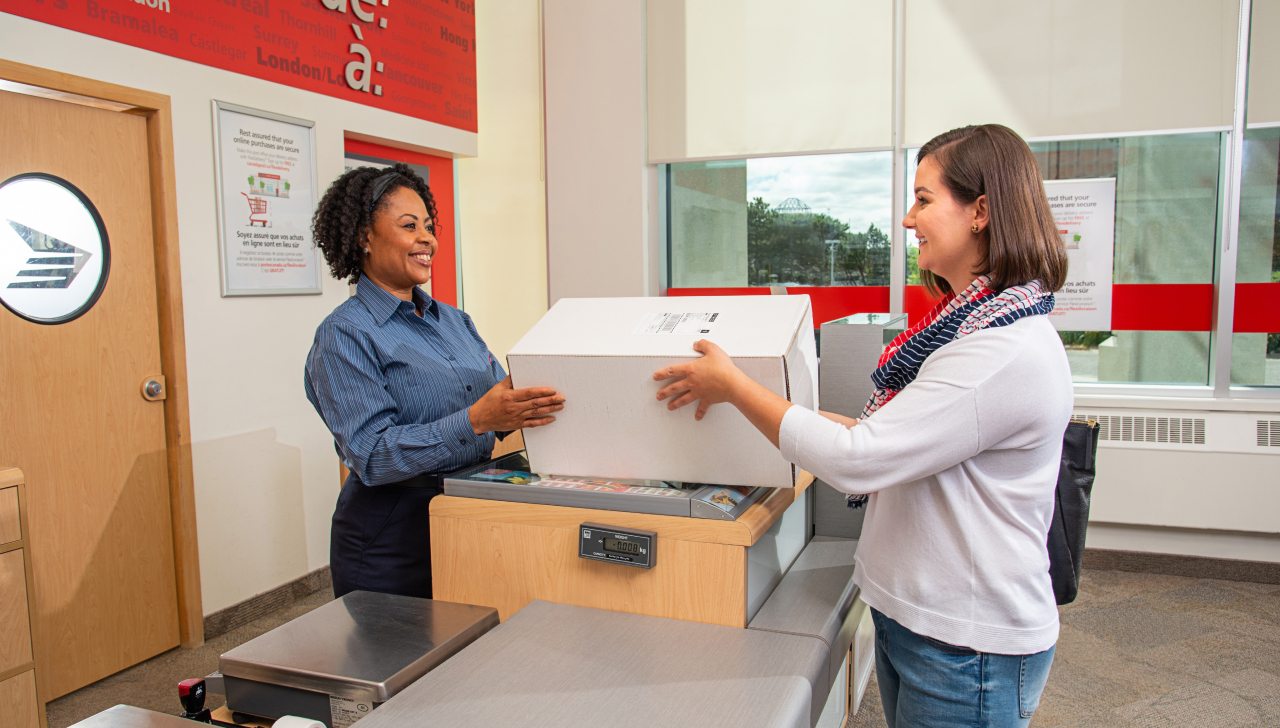 Une employée de Postes Canada sourit et remet un colis à une cliente souriante.