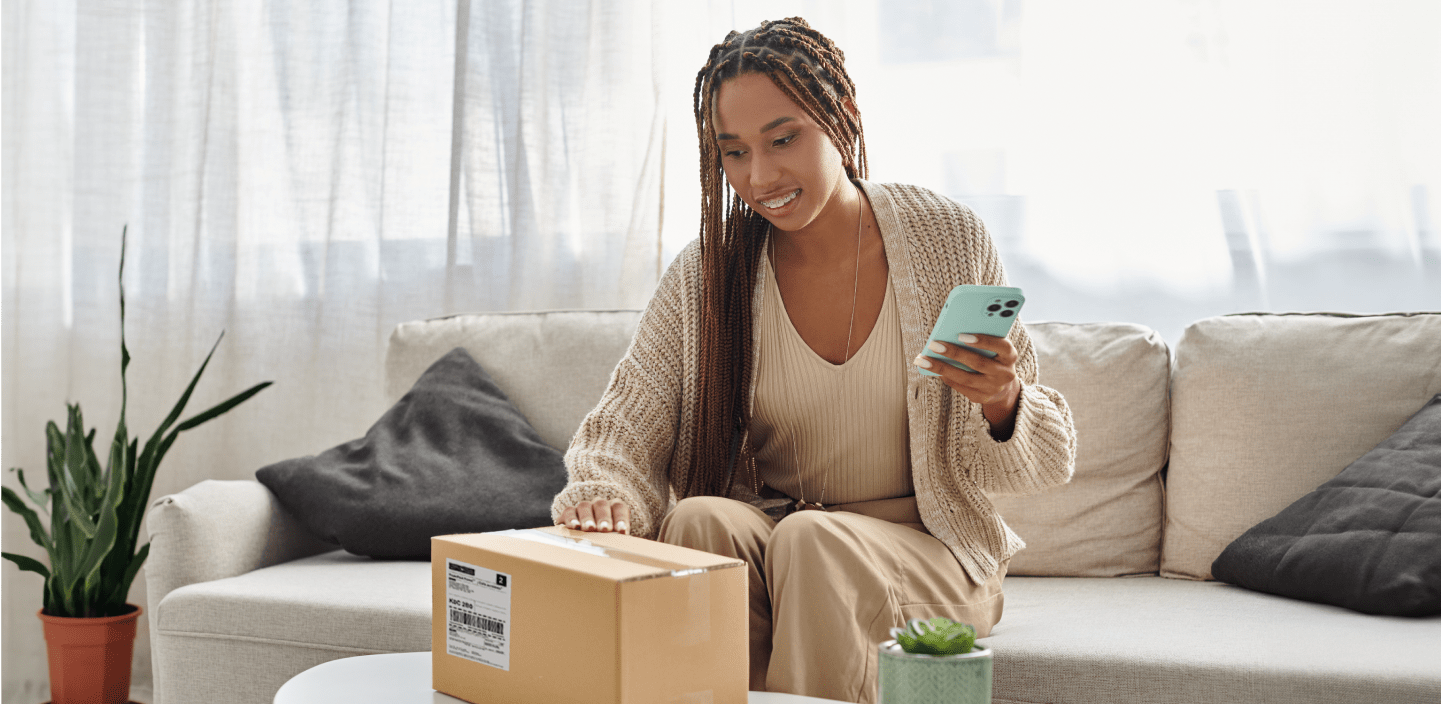 Une femme souriante regarde son téléphone intelligent en tenant un colis.