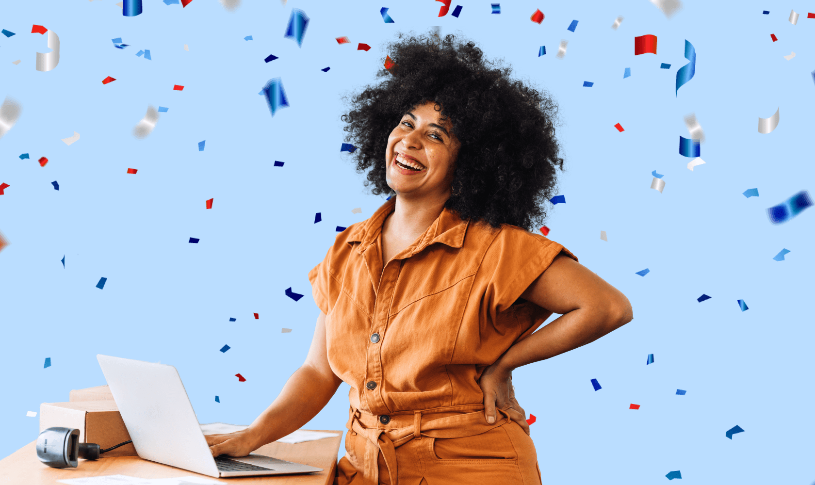 Une femme tout sourire vêtue d’une blouse orange manipule le clavier de son ordinateur portable à côté duquel se trouvent un colis et un balayeur optique.