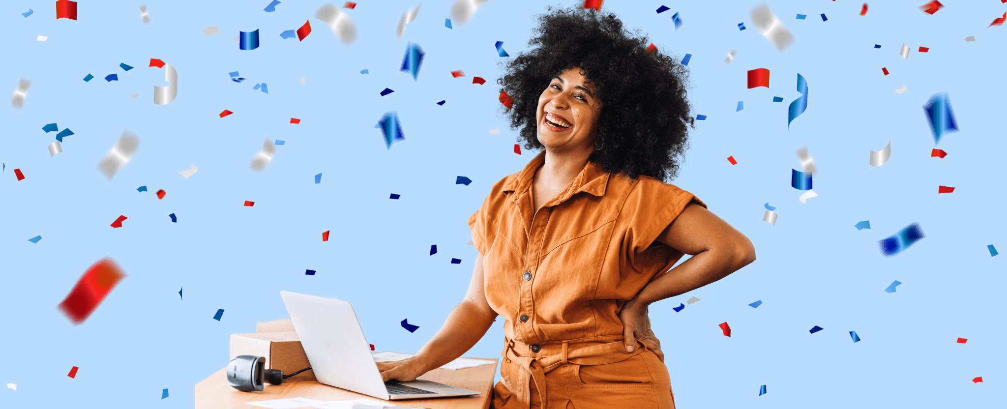 Une femme tout sourire vêtue d’une blouse orange manipule le clavier de son ordinateur portable à côté duquel se trouvent un colis et un balayeur optique.