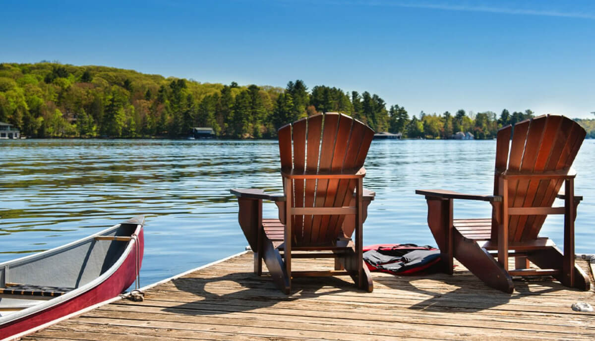 Deux chaises en bois reposent sur un quai au bord d’un lac, à côté d’un canot.