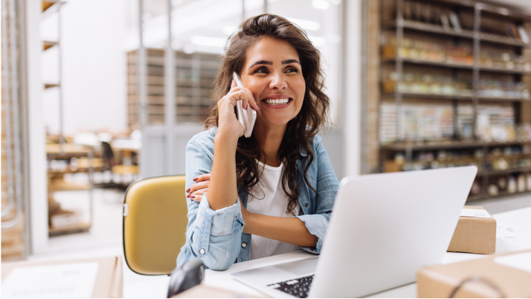 Une femme assise à un bureau devant un ordinateur portable parle sur un téléphone cellulaire.